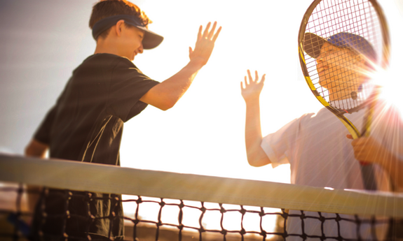 Zwei jugendliche Tennisspieler stehen am Netz und klatschen sich mit den Händen ab