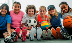 Kinder sitzen auf der Sporthalle auf dem Boden mit Bällen