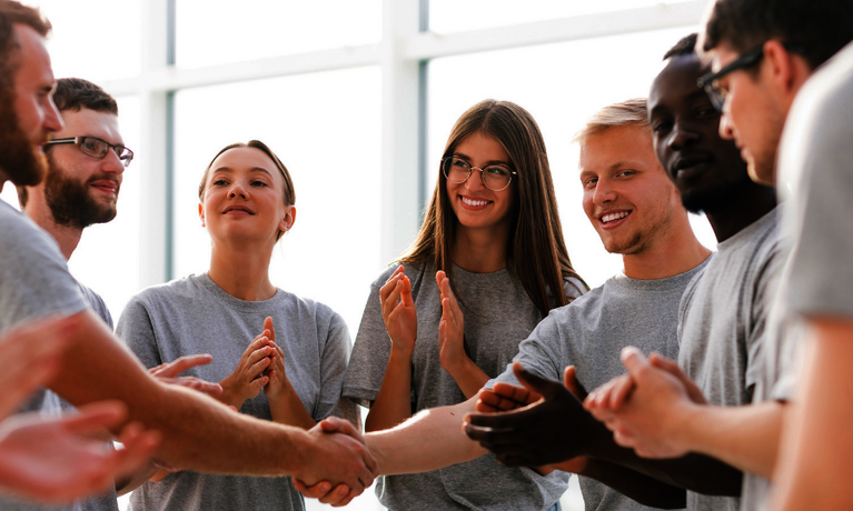 Eine Gruppe von jungen Menschen gibt sich im Kreis die Hand